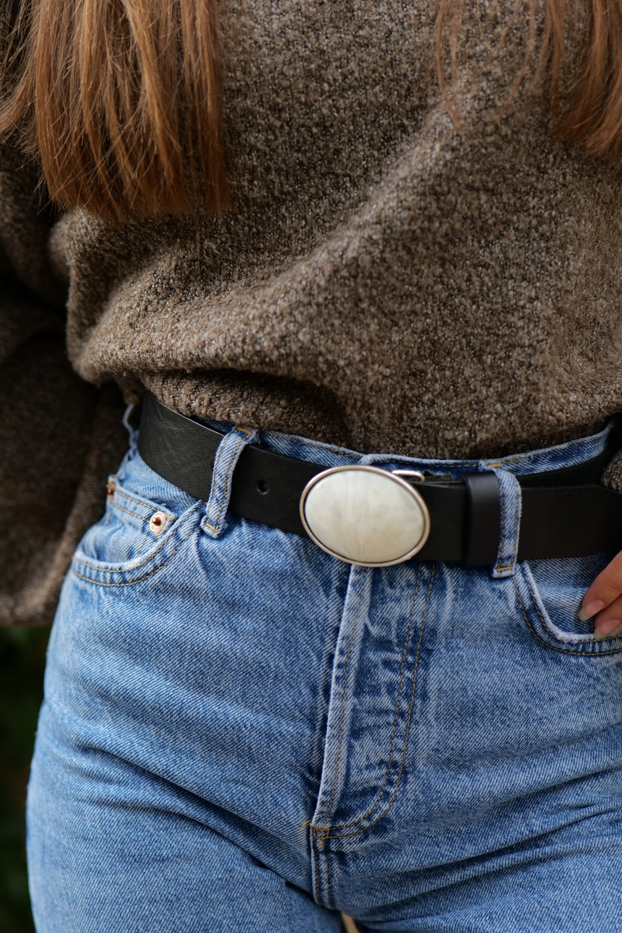 Femme portant la ceinture Suzanne en cuir noir avec plaque blanche sur un jean