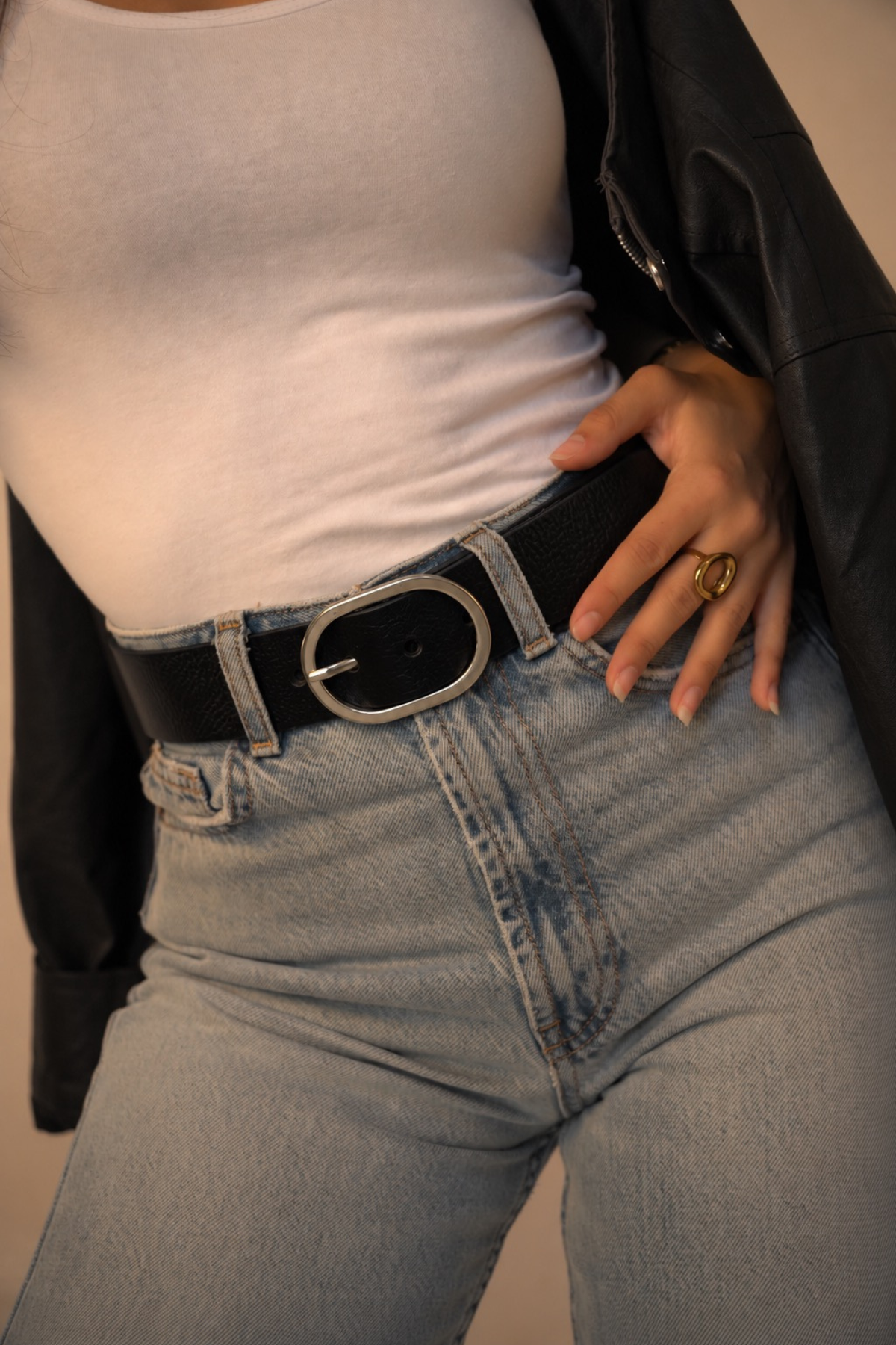 Détail de la ceinture large Louise Atelier Nappa : cuir de vachette noir et boucle ovale argentée brillante sur un jean clair