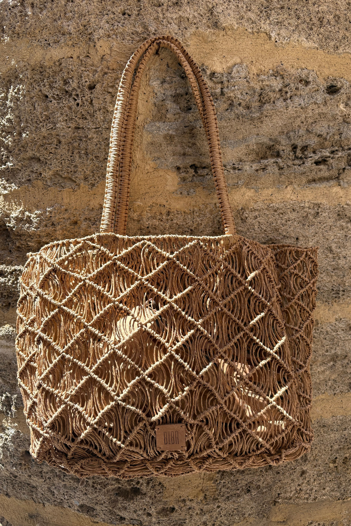 Grand sac cabas raphia macramé Sodwana XL naturel camel Biba sur mur de pierre
