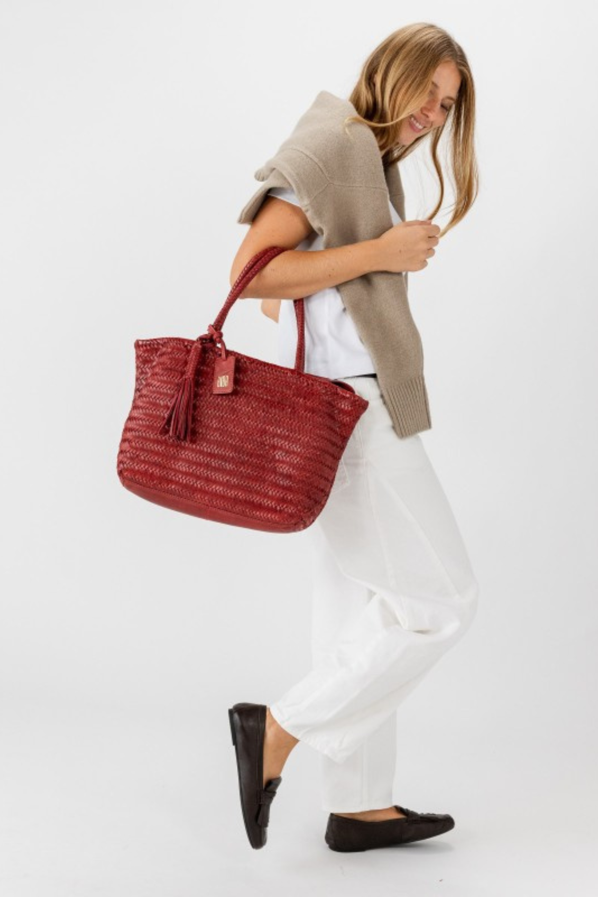 Sac cabas en cuir tressé bordeaux Biba Perkins porté à l’épaule avec un jean blanc