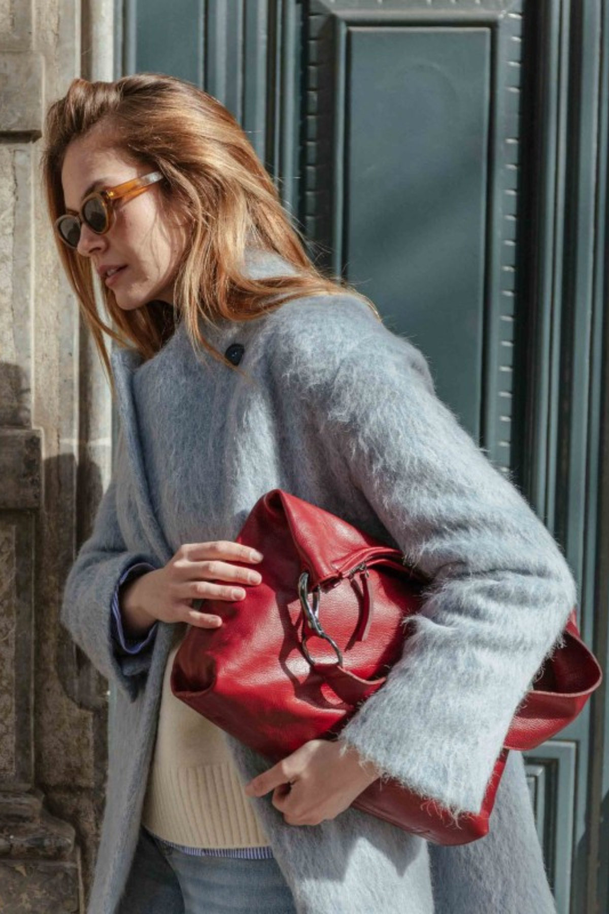 Sac hobo en cuir bordeaux Biba Jackpot porté sous le bras avec un manteau gris, mousqueton métal argenté