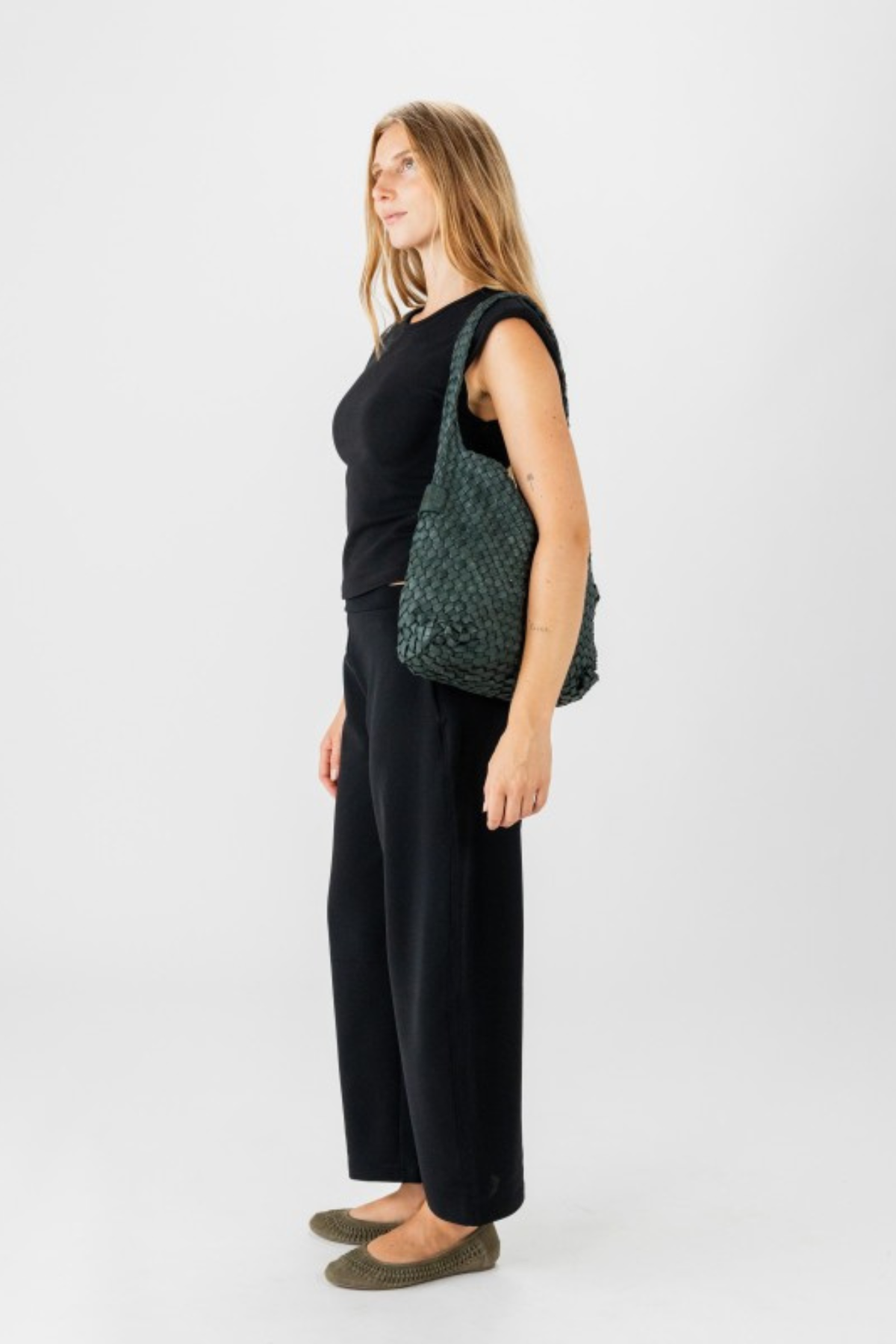 Sac hobo en cuir tressé vert foncé Biba Killen porté à l’épaule avec une tenue noire