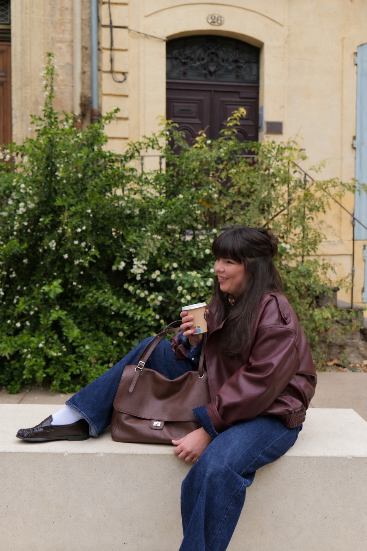 Sac à rabat en cuir grainé Margot format moyen posé à côté d’une femme assise, tenue jean