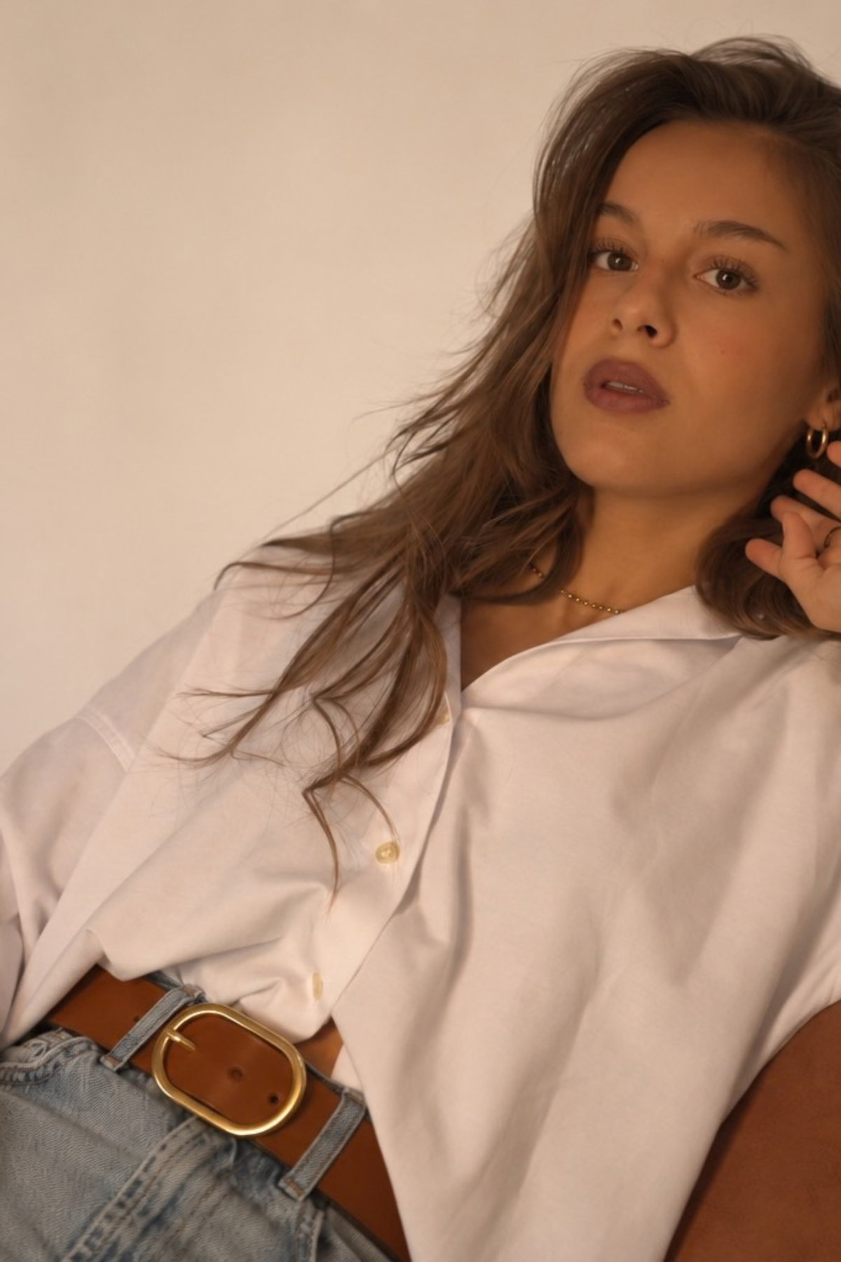 Ceinture Louise Atelier Nappa en cuir cognac à boucle ovale dorée, portée sur un jean avec une chemise blanche oversize