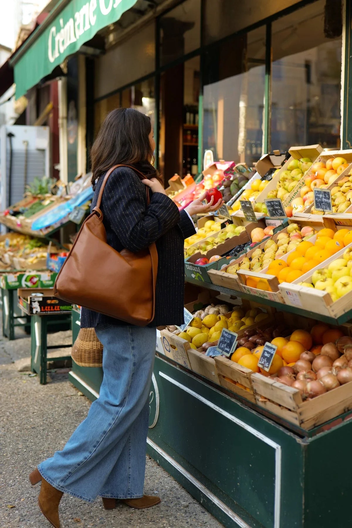Sac Jérôme en cuir grainé camel porté en sac à main devant une épicerie